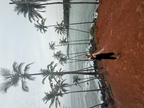 Person posing with palm trees by the ocean.