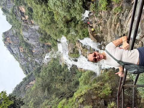 Person smiling in front of a large waterfall.