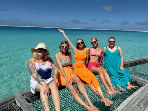 Group of women posing on a wooden pier over crystal clear waters.