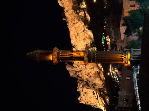       Illuminated tower against a rocky hillside at night.
  