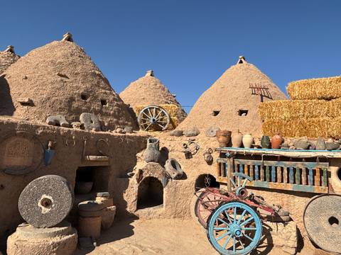 Traditional beehive mud huts with pottery and tools displayed outside.