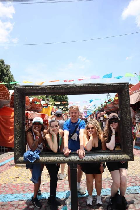       Group posing with a large frame in a colorful street market.
  