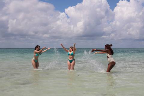       Three women playing in the ocean.
  