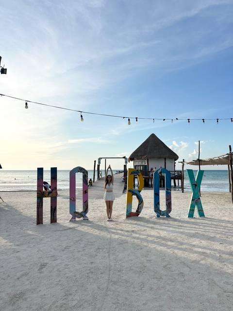       Woman posing with 'Holbox' sign on a beach.
  