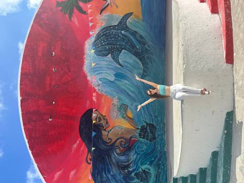       Woman sitting in front of a colorful mural with marine imagery.
  