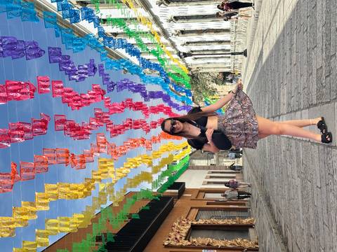       Woman posing under colorful papel picado decorations on a street.
  