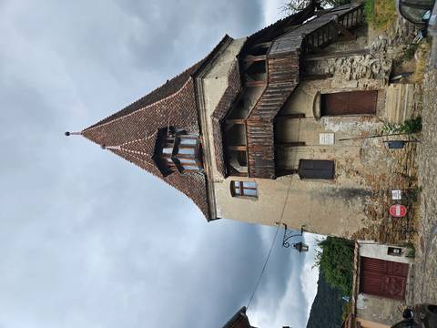 A tall historic building with a pointed roof and wooden balcony.