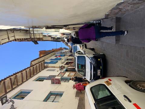       Narrow street with pedestrians and cars, flags displayed.
  