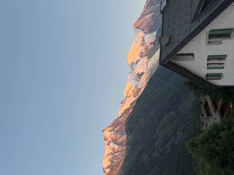 Sunrise over mountain peaks with a house roof in the foreground.