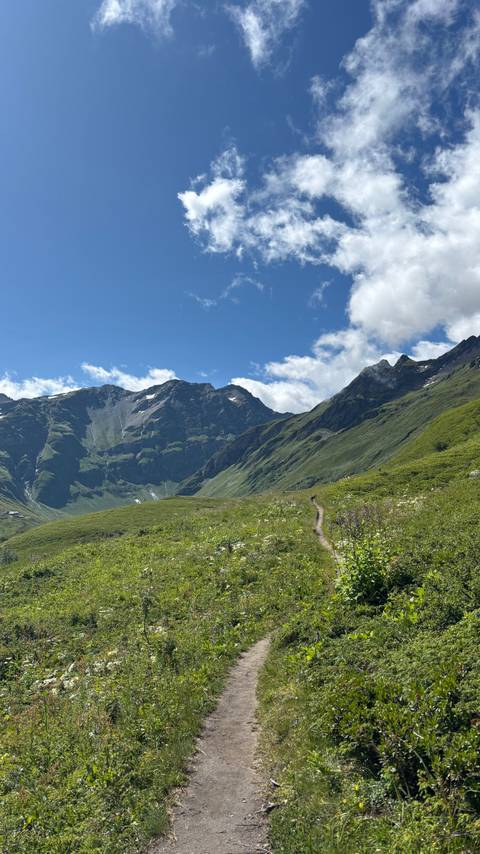 Green mountains with a dirt trail leading into the distance.
