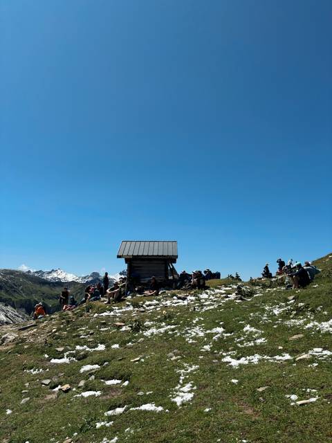 Group of people gathered around a modest shelter on a mountain.