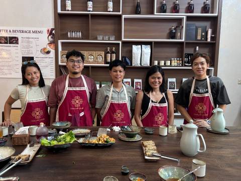 Five people wearing aprons posing in front of a table with food items.