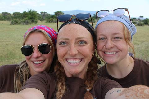 Close-up of three smiling women taking a selfie in a grassy area.