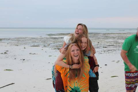      Friends playfully posing on a sandy beach with shallow water.
  