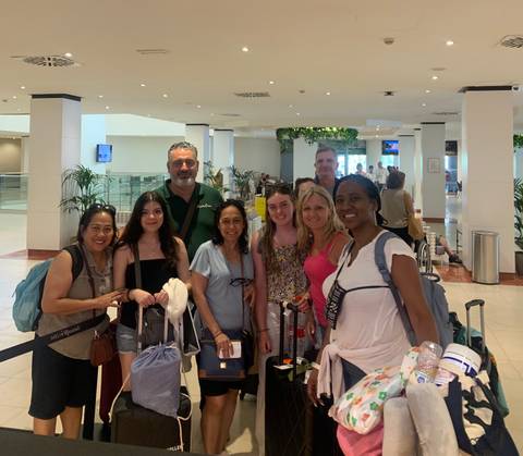 A group of people posing happily together in an indoor setting with luggage around.