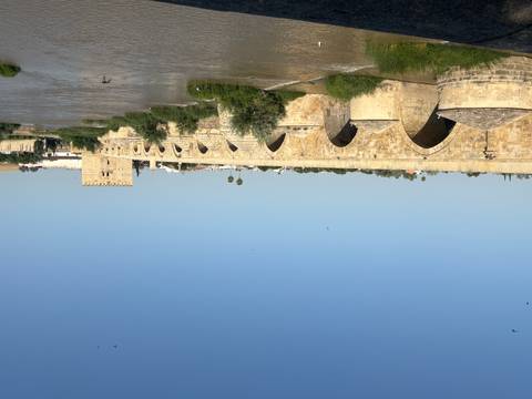       An ancient stone bridge over a river with a fortified gate.
  