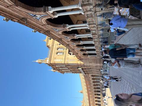 People walking around a historic plaza with arches and decorative tiles.
