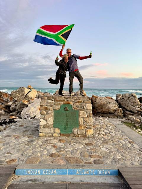       Two people posing happily on a rock platform with the ocean in the background.
  