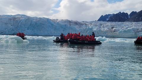 People in boats with life vests exploring a glacier area.