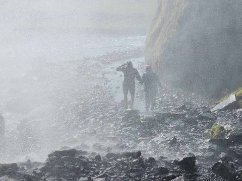 Two people walking near a misty waterfall