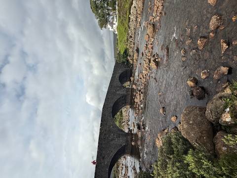       A stone bridge spanning a river with rocky banks.
  