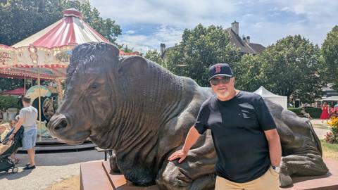       Man posing next to a large bull statue by a carousel
  