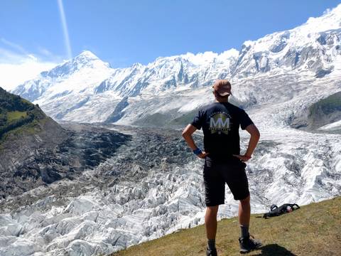 Person standing near a glacier with mountains in the background.