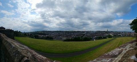       Panoramic view of a green field with a city in the background under cloudy skies.
  
