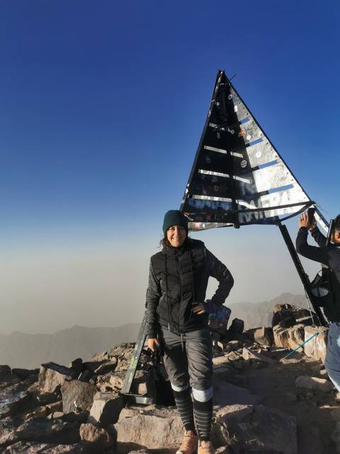 Woman posing at mountaintop with a unique structure.