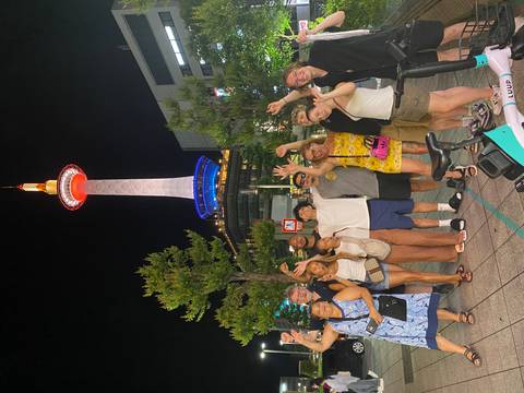 Group posing in front of a lit-up tower at night.