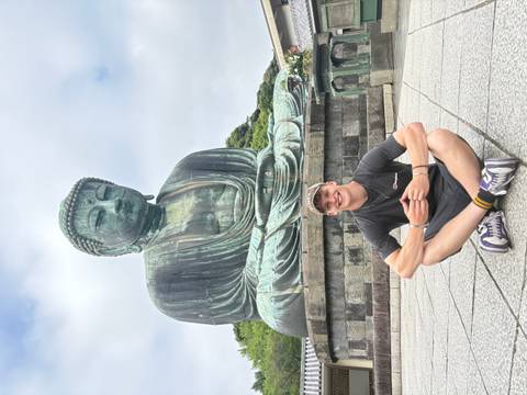       Person sitting in front of a giant Buddha statue.
  