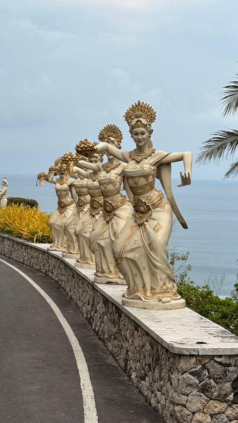       Statues of dancers with the ocean in the background.
  