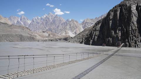 Hanging bridge over a river with striking mountains in the background.