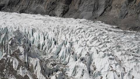 Close-up of jagged glacier surface with rocky backdrop.