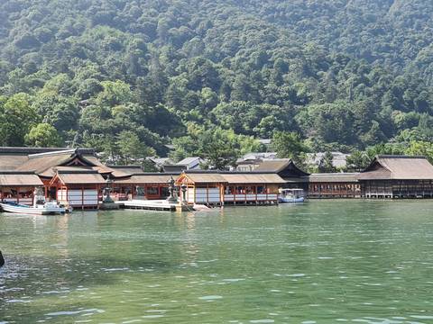       Traditional Japanese shrine buildings over the water with a forested mountain backdrop.
  