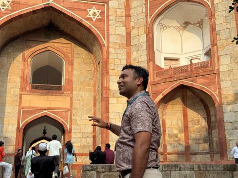 Man standing in front of an architectural design with red sandstone and arches.