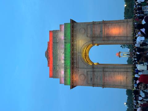 India Gate lit up with colorful lights and a crowd in front.
