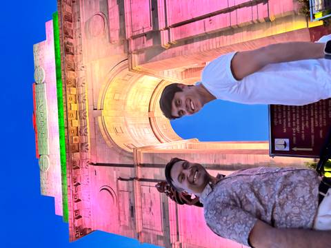 Two men posing in front of India Gate at night.