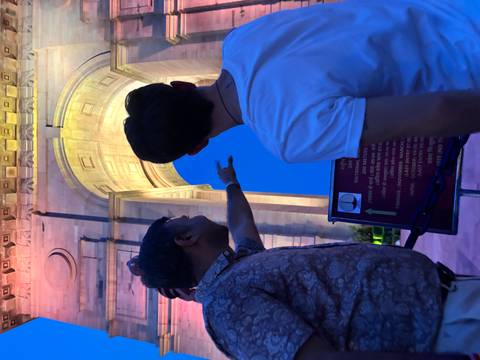 Two men pointing at India Gate illuminated at night.