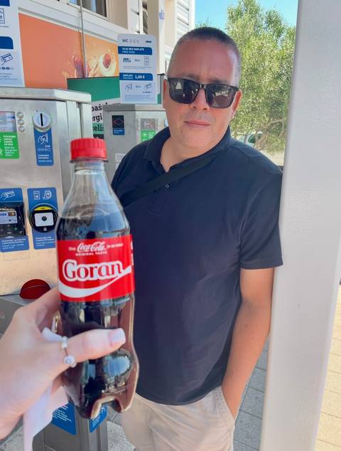       Person holding a Coca-Cola bottle with a name label.
  