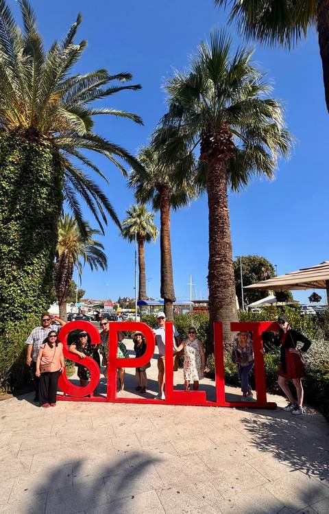       Group of people posing in front of large letters and palm trees.
  