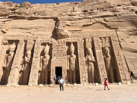 Tourists visiting Abu Simbel temples with large statues engraved on rock face.
