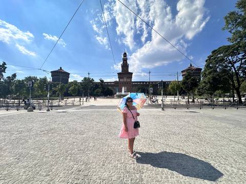       Woman with umbrella near historic building under blue sky.
  
