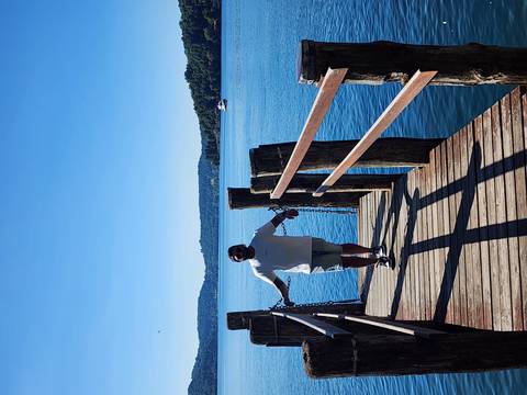       Person standing on a wooden pier with water and hills.
  