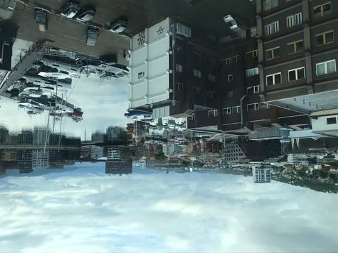       View of a harbor with boats and buildings, cloudy sky reflecting on water.
  