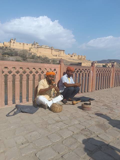 Two men in traditional attire playing instruments at a historic fort.