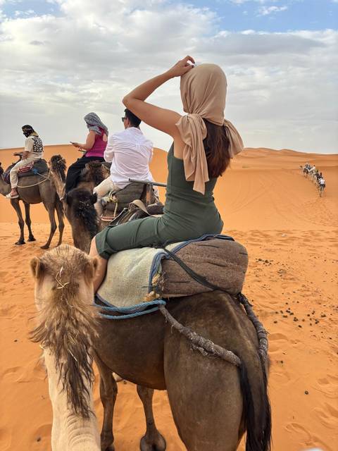       Person on camel in desert with a group in the background.
  