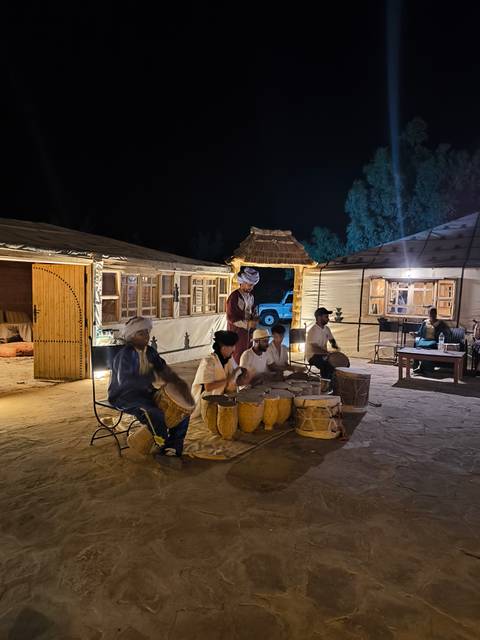      Group of people playing drums at night in a camp.
  