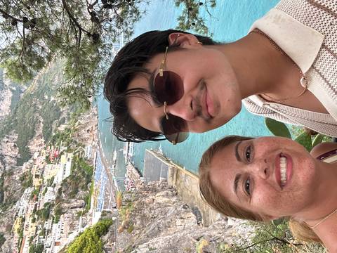 Two people posing with a scenic view of Positano coastline in the background.