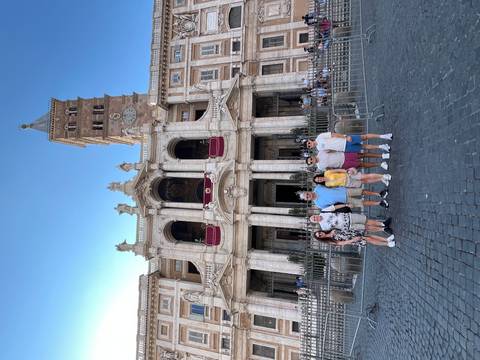       People posing in front of a grand building with a clock tower.
  
